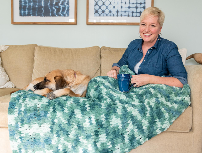 woman sitting on couch with mug, finger knit blanket, and dogs