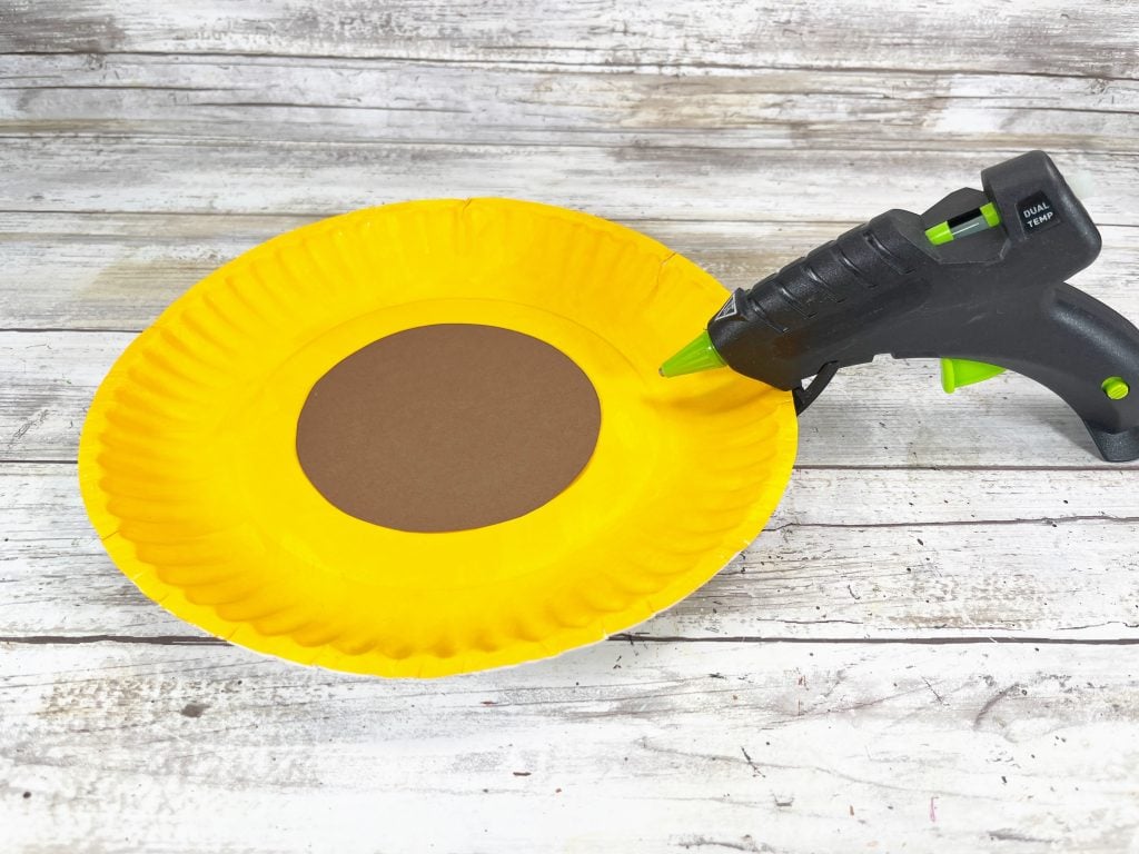 hot gluing brown circle to yellow paper plate