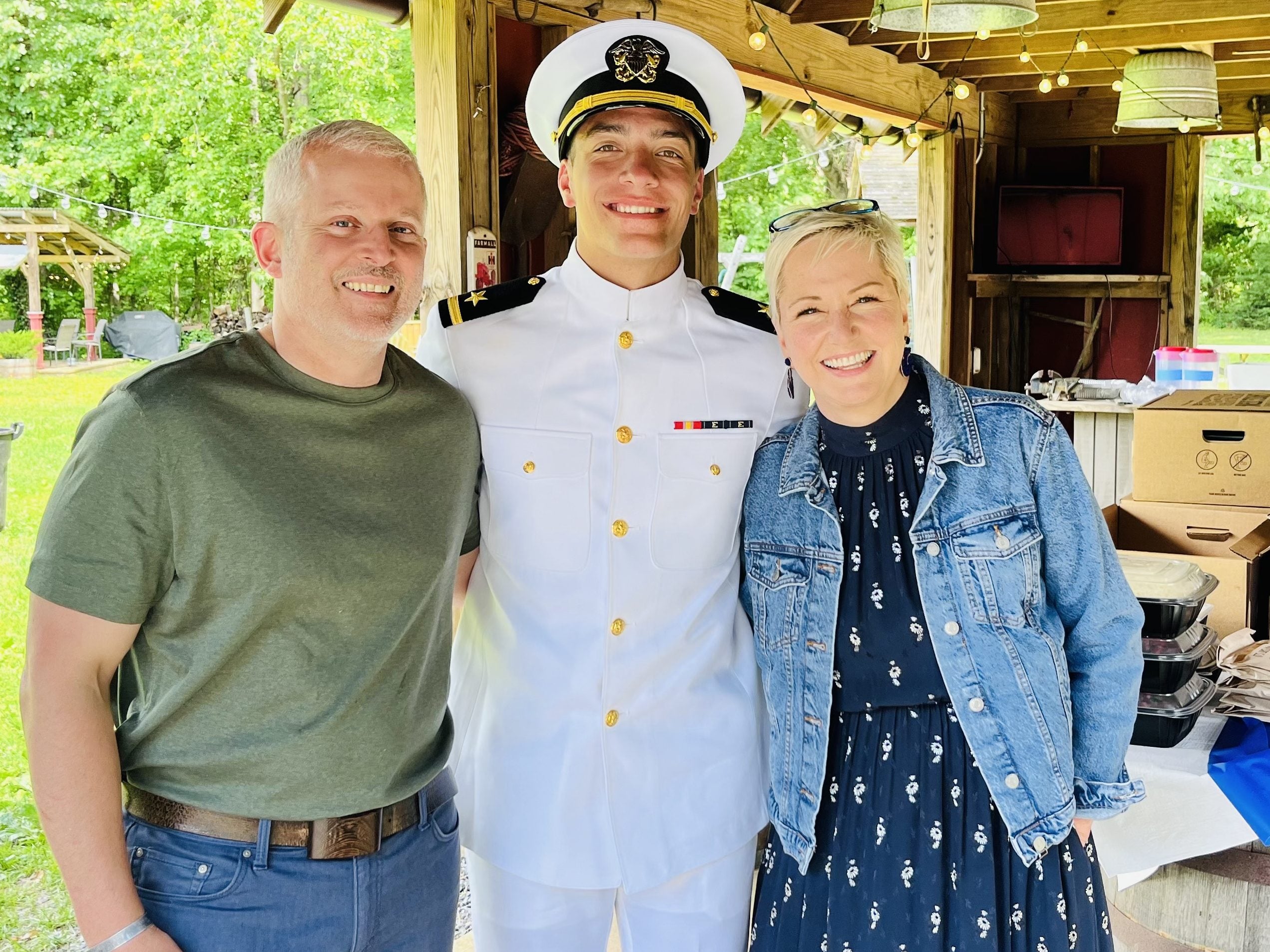 couple smiling at camera with man in naval military uniform in the middle